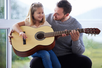 Sticker - She loves learning from dad. a young father teaching his daughter to play the guitar at home.