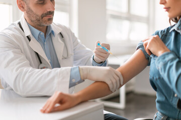 Wall Mural - Vaccination concept. Young woman getting vaccinated against viruses in hospital, male doctor giving vaccine injection