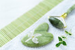 Spa composition of green jade Gua sha and roller, white flower, small branch of green leaves on the white towel and green bamboo napkin. Freshness. Flat lay 