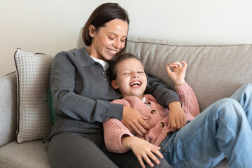 Wall Mural - Cheerful european millennial mom hugging little girl, tickling, have fun together, enjoy spare time