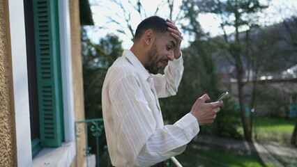 One excited Arab young man reacting with unbelief to positive message on cellphone device while standing outside at balcony during sunny day