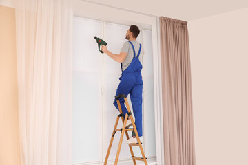 Wall Mural - Worker in uniform installing roller window blind on stepladder indoors