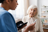 Fototapeta  - multiracial nurse holding lancet pen and explaining how to use it to senior woman with grey hair.