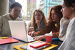 © CarlosBarquero - Serious diverse friends study together with laptop. Classmates prepare exam drinking coffee outside campus. Focused group of young multiracial people using computer sitting on the terrace of cafeteria