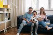 © cherryandbees - Family of 3 is sitting on the sofa and watching a football game