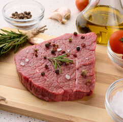 Wall Mural - Raw piece of beef with spices pepper, rosemary sprig, salt and olive oil on a wooden board, top view