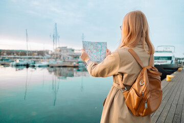 Young adult tourist woman reading map hiking trip looking to find place to go on the pier near the expensive yachts 