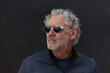© Diane - Color portrait of an attractive older Caucasian man with grey hair and beard, wearing sunglasses. Looking to the side with a serious expression. Low key, dark background.