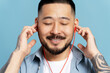 Portrait of handsome smiling asian man with eyes closed, wearing red headphones listening music isolated on blue background. Technology, positive lifestyle concept  