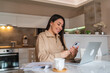© Dusan - A young woman is working from her kitchen using laptop drinking coffee and using mobile phone