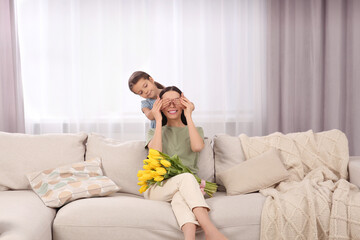 Wall Mural - Daughter gifting happy woman bouquet of yellow tulips at home. Mother's day celebration