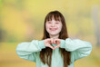 Happy young girl with Downs syndrom shows heart sign at summer park