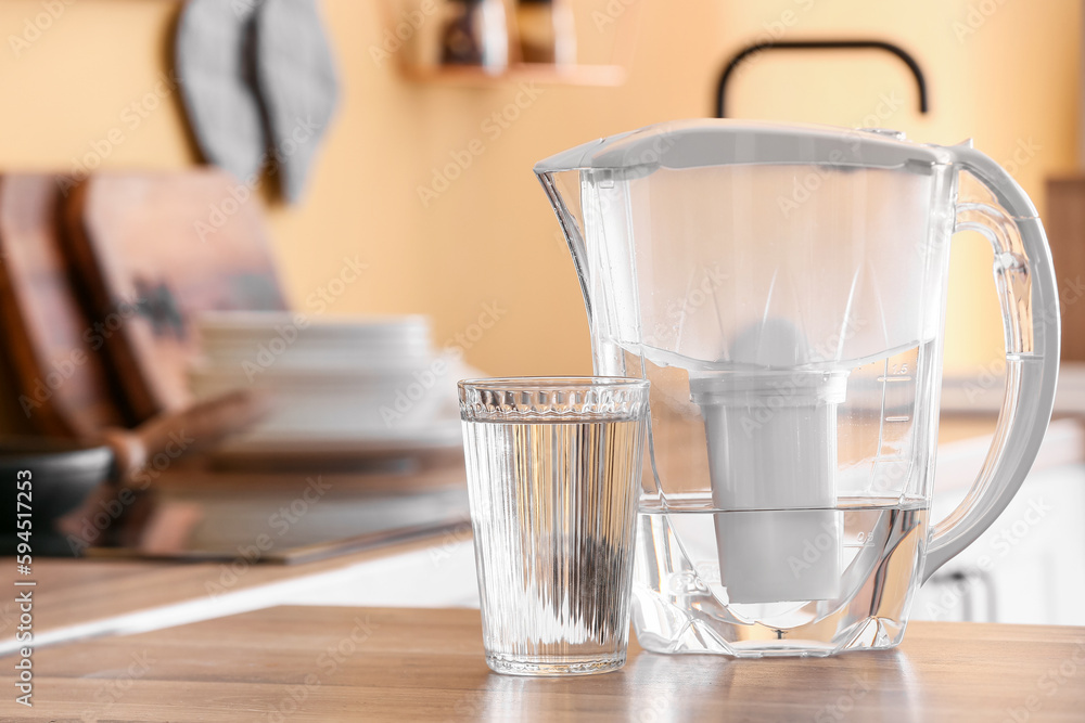 Modern filter jug and glass of water on kitchen counter