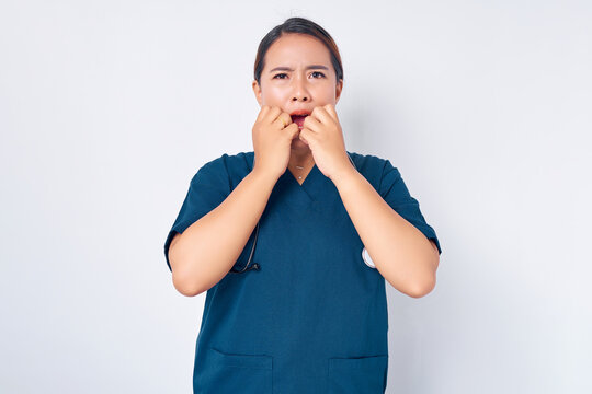 Scared insecure young Asian female nurse working wearing blue uniform panic from fear and bitting nail and looking horrified isolated on white background. Healthcare medicine concept