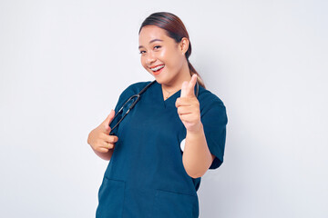 Wall Mural - Cheerful young Asian female professional nurse working wearing a blue uniform pointing at camera, making happy choice isolated on white background. Healthcare medicine concept