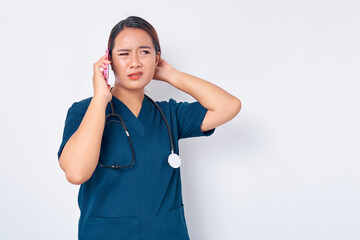 Wall Mural - Beautiful young Asian woman professional nurse working wearing a blue uniform talking on mobile phone, looking aside with confused facial isolated on white background. Healthcare medicine concept