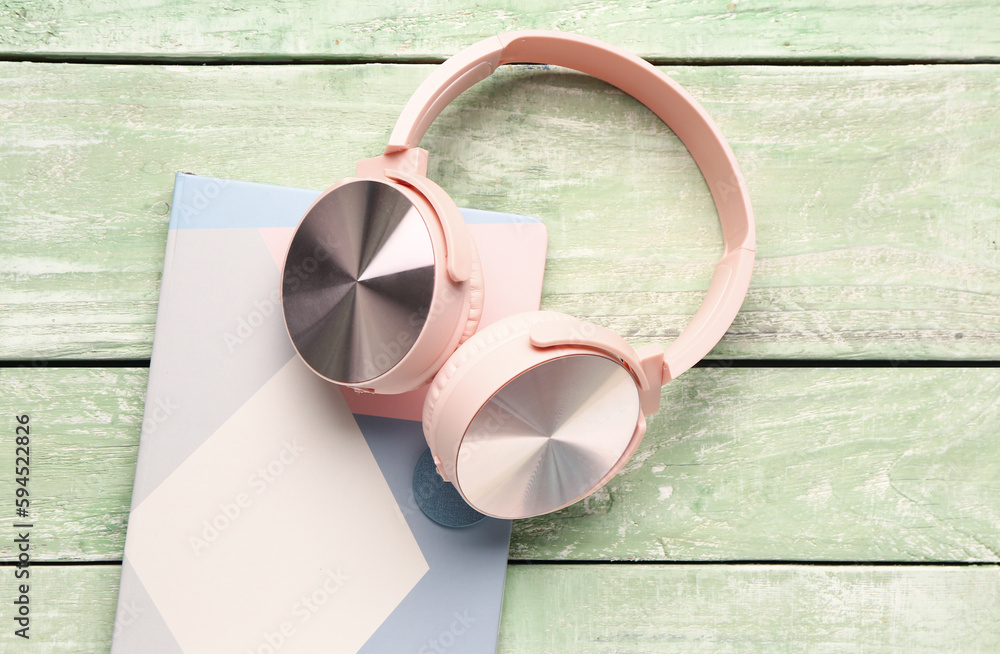 Headphones with notebook on green wooden background