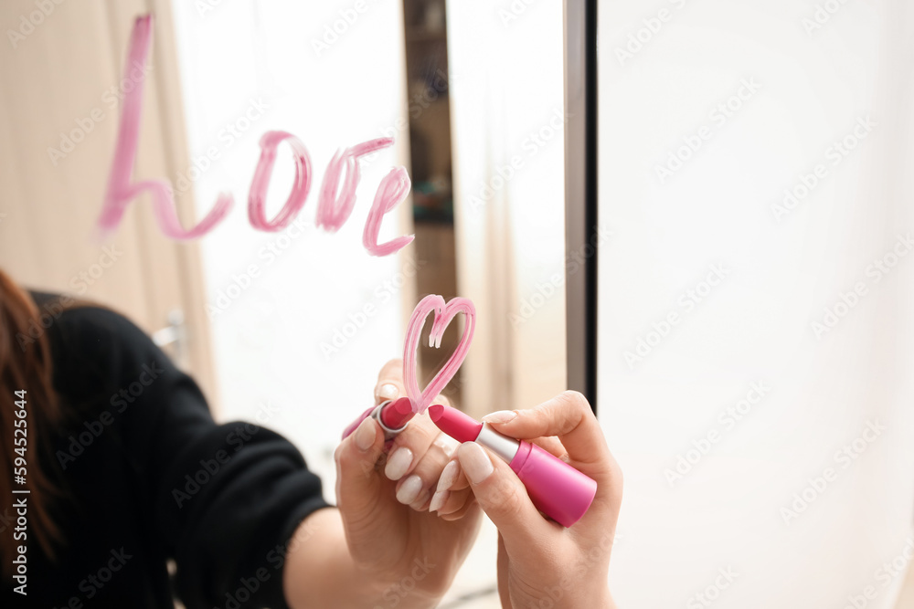 Woman writing word LOVE with lipstick on mirror
