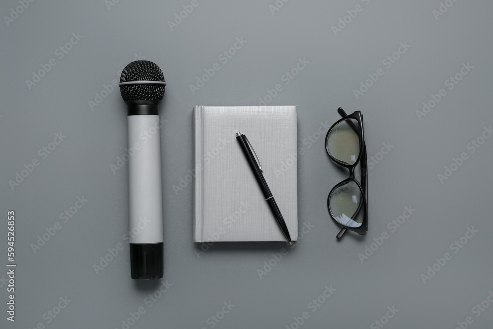 Notebook with pen, microphone and eyeglasses on dark background