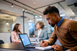 © Drazen - Black male entrepreneur using laptop while writing notes during business meeting in office.