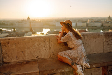 Smiling female tourist in a hat admires the landscape of the city at dawn. Euro-trip. Travel, tourism and active lifestyle concept.