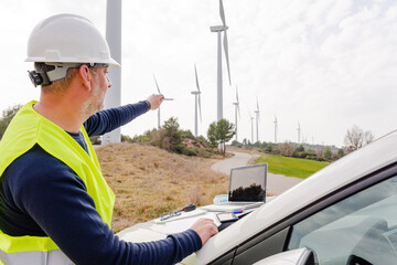 electrical engineer pointing at blueprint of wind turbine to perform maintenance of windmill in wind farm
