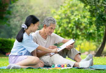 Wall Mural - portrait asian senior man and girl teen sitting in the park, grandfather and granddaughter spend free time together by drawing, concept family lifestyle,relationship,activity,hobbies,holidays,raising 