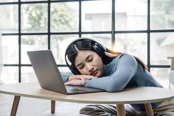 Tired teenage asian female student fell asleep at her desk, resting her head on her hand, during a lecture in home, taking a break, closed her eyes and relaxing
