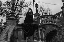 A Woman In A Black Dress Standing On A Set Of Stairs With Her Hands In Her Pockets And Her Eyes Closed, A Matte Painting, Gothic Art