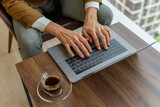 Fototapeta  - Close up of a businessman hand over the keyboard of a laptop on a desk with a cup of coffee