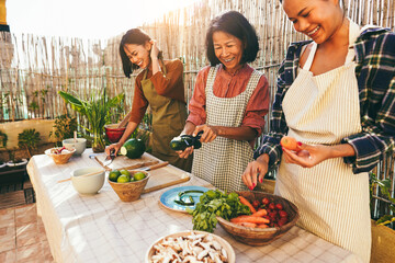 Wall Mural - Asian family cooking together at home patio outdoor - Mother and two daughters having fun preparing dinner at house backyard - Main focus on center woman face