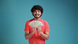 © Виталий Лысак - Smiling cheerful happy young bearded Indian man 20s years old wears coral shirt holding showing fan of cash money in dollar banknotes looking camera isolated on plain blue background studio portrait