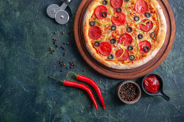 Wall Mural - Homemade pizza on wooden cutting board and pepper ketchup on the left side on isolated dark background