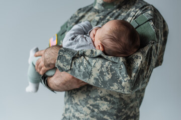 Poster - cropped view of serviceman in uniform holding newborn baby isolated on grey.