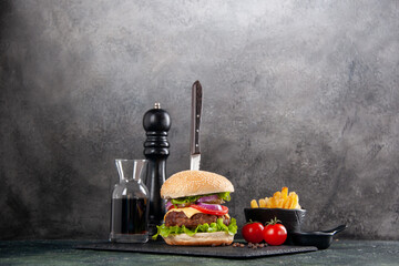 Knife in delicious meat sandwich and green pepper on black tray sauce ketchup tomatoes with stem fries on gray background