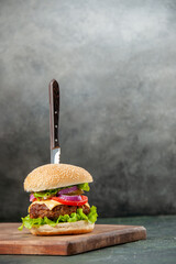 Wall Mural - Knife in delicious meat sandwich on wooden cutting board on isolated dark background