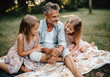 © LunaLu - An aged father with little daughters are relaxing in park. Happy father's day. Happy family picnic. Ai generated.