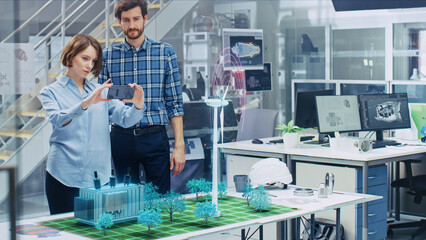 Wall Mural - green energy concept: two eco-engineers use augmented reality smartphone to design 3d wind turbine p