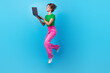 © deagreez - Full length photo of shiny adorable woman dressed green top jumping high texting modern gadget isolated blue color background