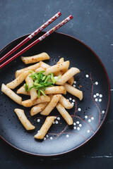 Wall Mural - Black plate with korean traditional tteokbokki or rice cakes, vertical shot on a black marble background, high angle view