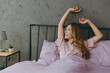 © ViDi Studio - Young satisfied happy woman wear purple t-shirt pajama lying in bed rest relax spend time in bedroom lounge home in own room hotel wake up dream be lost in reverie good mood day. Real estate concept.