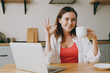 © ViDi Studio - Young happy fun housewife IT woman wears casual clothes hold use working on laptop pc computer dink coffee show okay ok eat breakfast cooking food in light kitchen at home alone. Healthy diet concept.