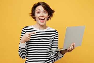 Wall Mural - Young surprised happy amazed IT woman wears casual striped black and white shirt hold use work point on laptop pc computer isolated on plain yellow color background studio portrait. Lifestyle concept.