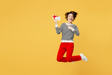 Wall Mural - Full body young fun woman wear casual black and white shirt jump high hold point on gift certificate coupon voucher card for store isolated on plain yellow color background studio. Lifestyle concept.