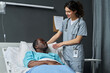 © AnnaStills - Young nurse in uniform caring about elderly patient while he lying on bed in hospital ward