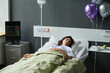 Young woman sleeping on bed in hospital ward decorated with balloons