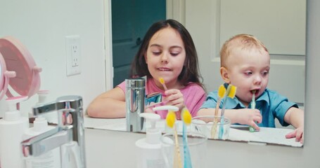 Two cheerful children brushing their teeth while holding a toothbrush while smiling at mirror in bathroom.Baby boy little girl learn how take care their teeth from childhood 