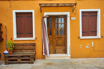 Wall Mural - Door and windows with flowers on the yellow facade of the house. Colorful architecture in Burano island, Venice.