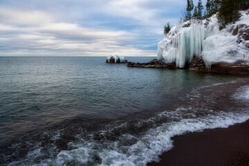 Canvas Print - an icy lake with ice crystals on the shore and rocks sticking from it