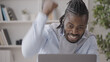 © Synthex - Black businessman celebrating great news, gesturing yes in front of laptop